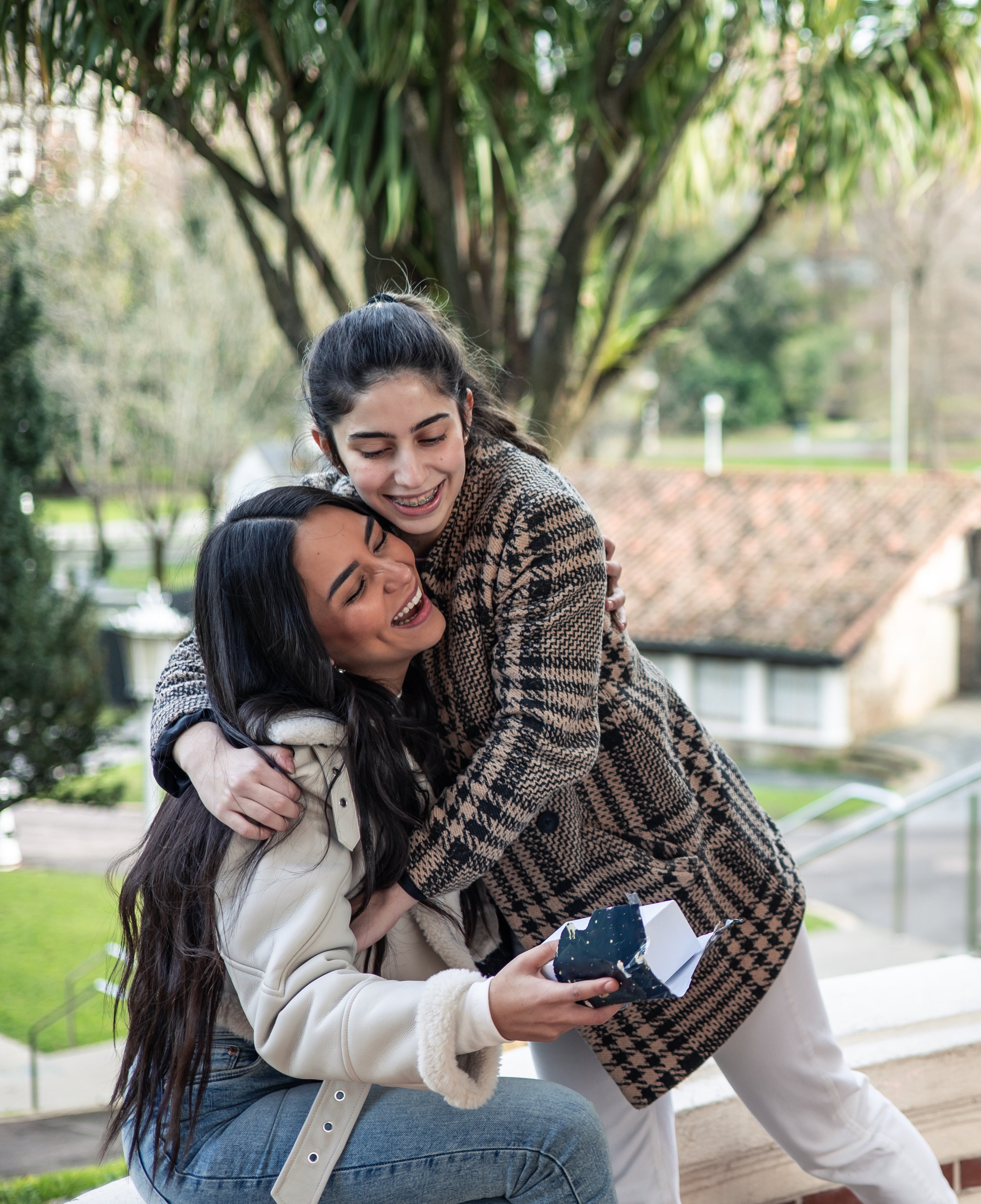Two women hugging outdoors with a park-like setting in the background