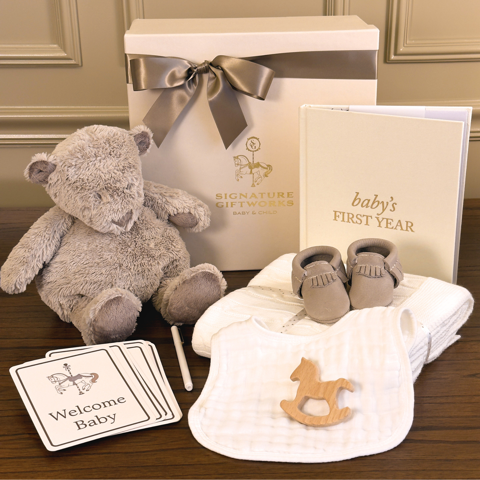 Baby gift set with teddy bear, shoes, blanket, and cards on a wooden surface.