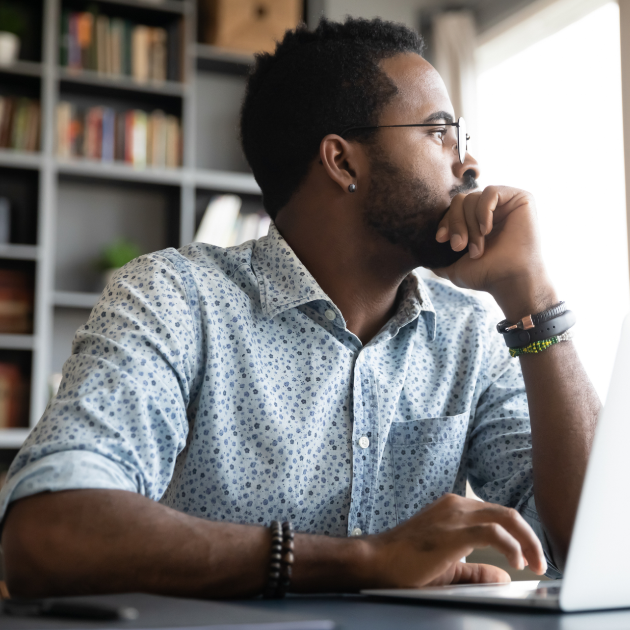 Man sitting at a desk with a laptop, looking thoughtful.
