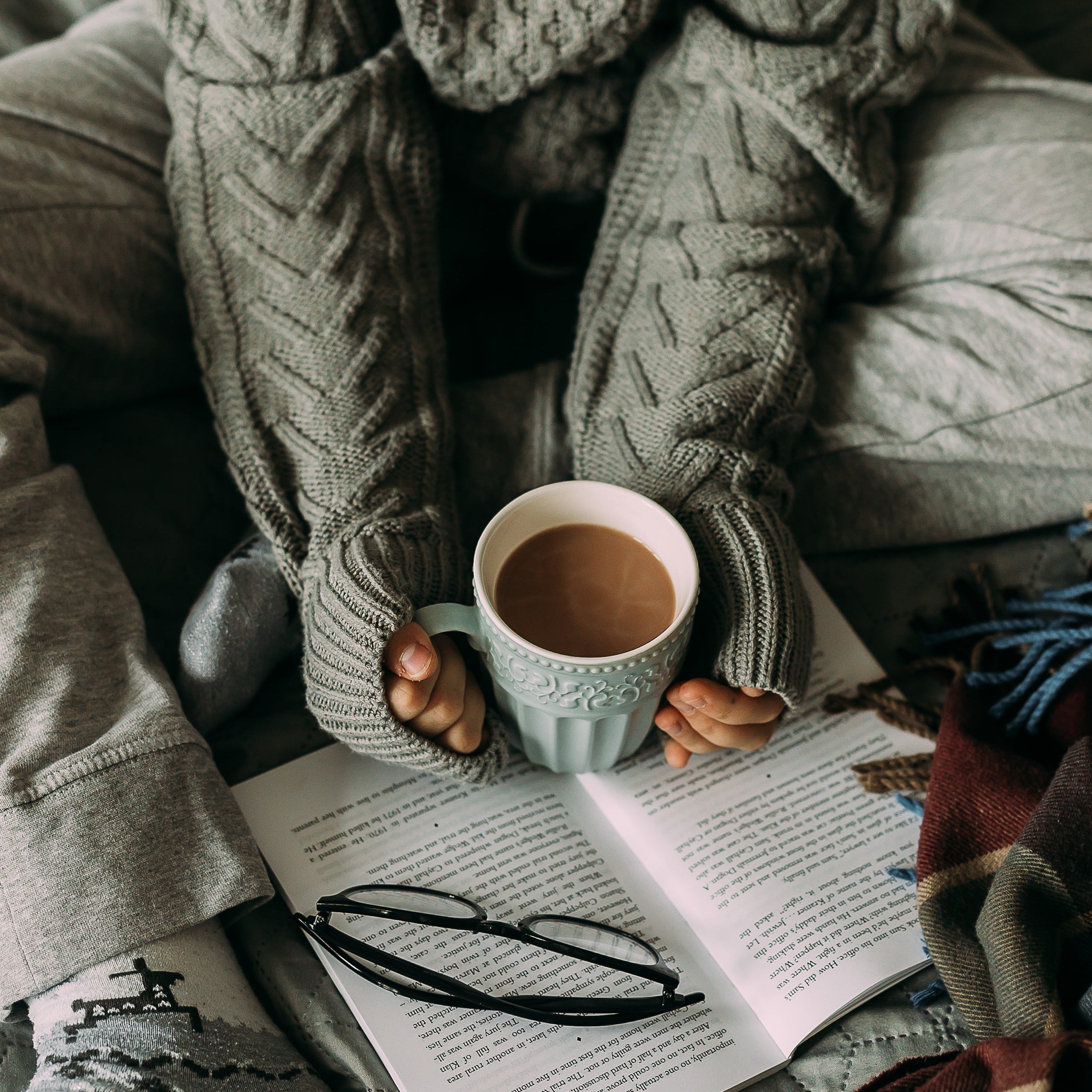Person in cozy robe holding a mug with a book open on a blanket