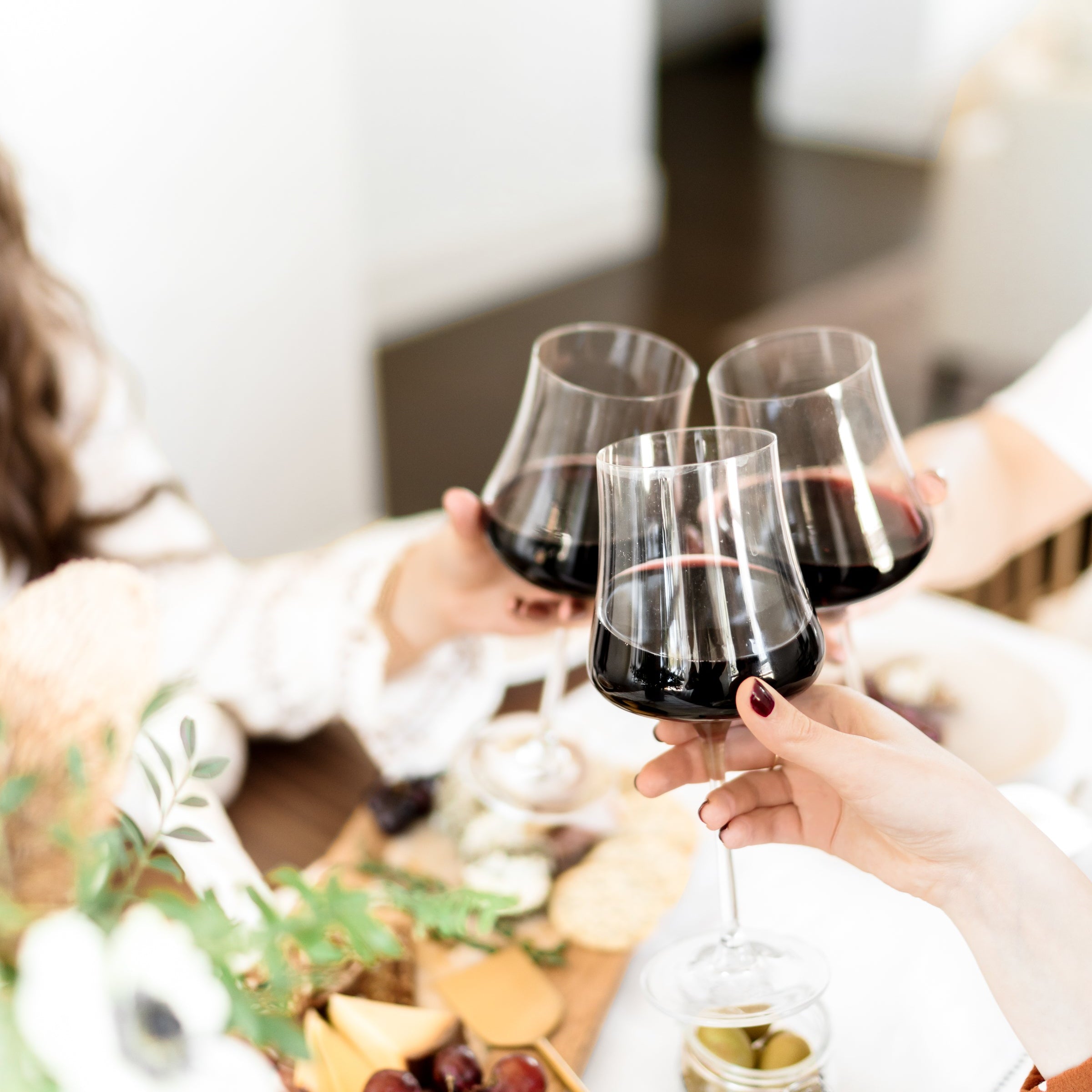 People toasting with red wine glasses at a table set for a meal.