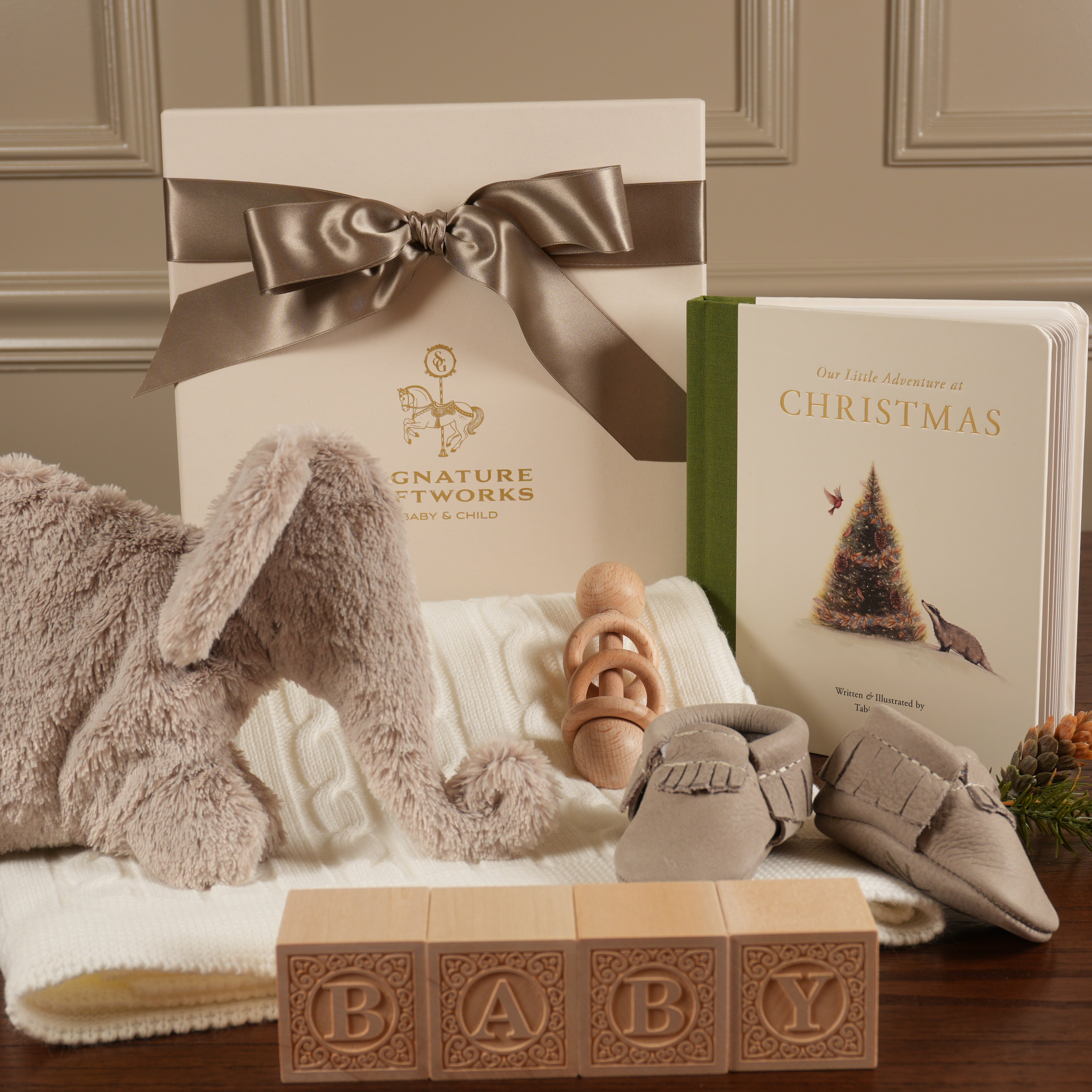 Baby gift set with plush toy, book, and blocks on a wooden surface.