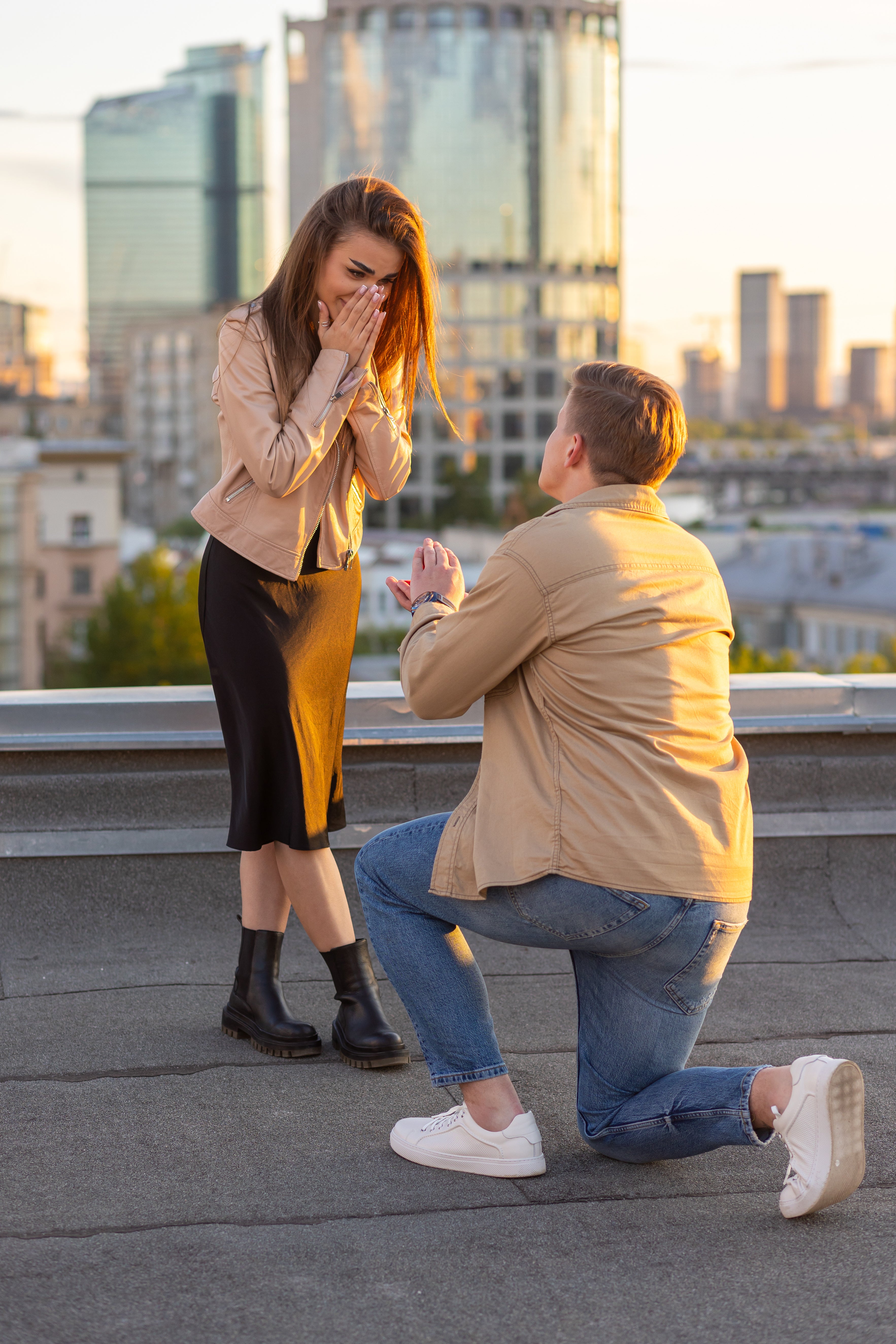 Man proposing to a woman on a rooftop with cityscape in the background