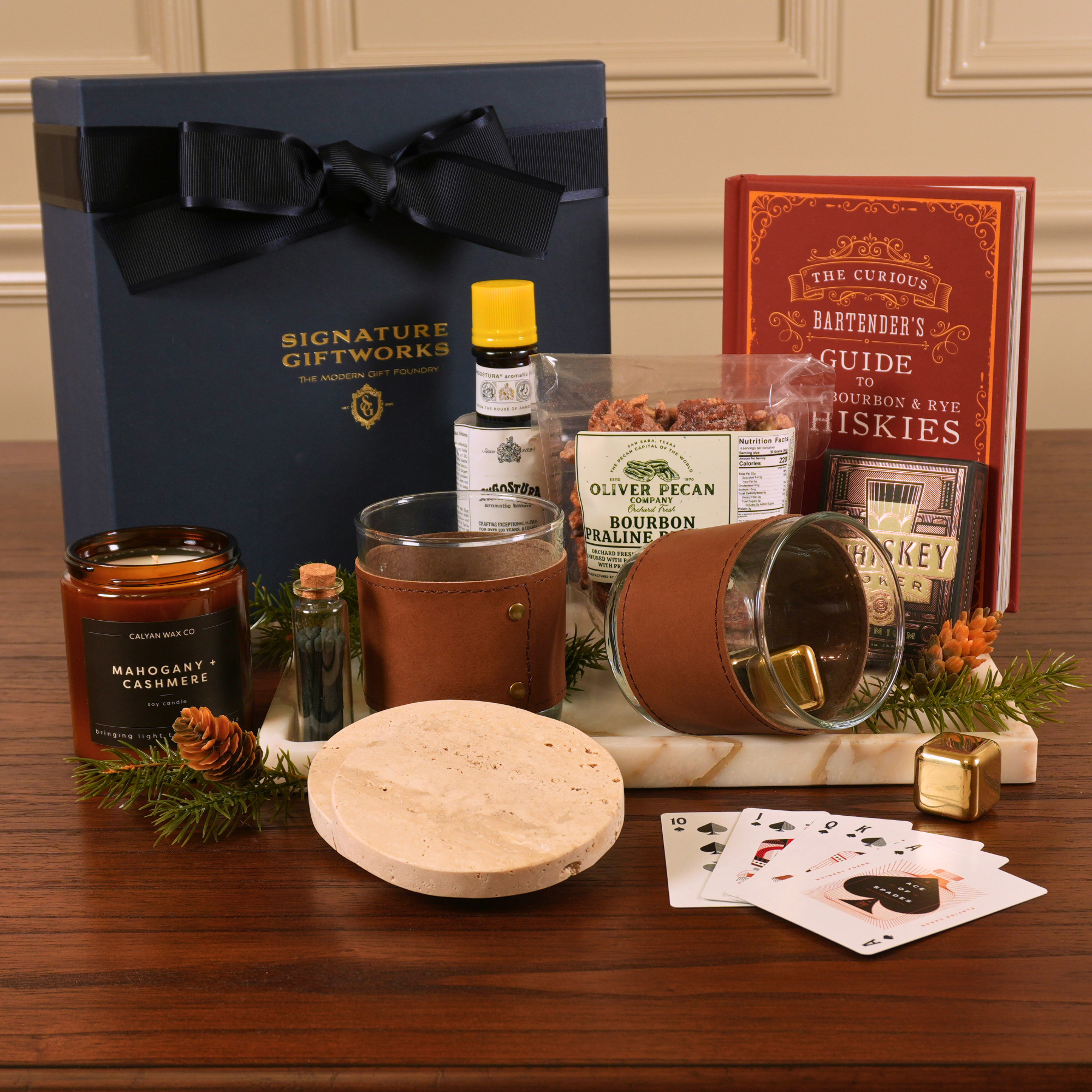 Gourmet gift set of glasses, playing cards, a book, a candle, and decorative items on a marble tray.