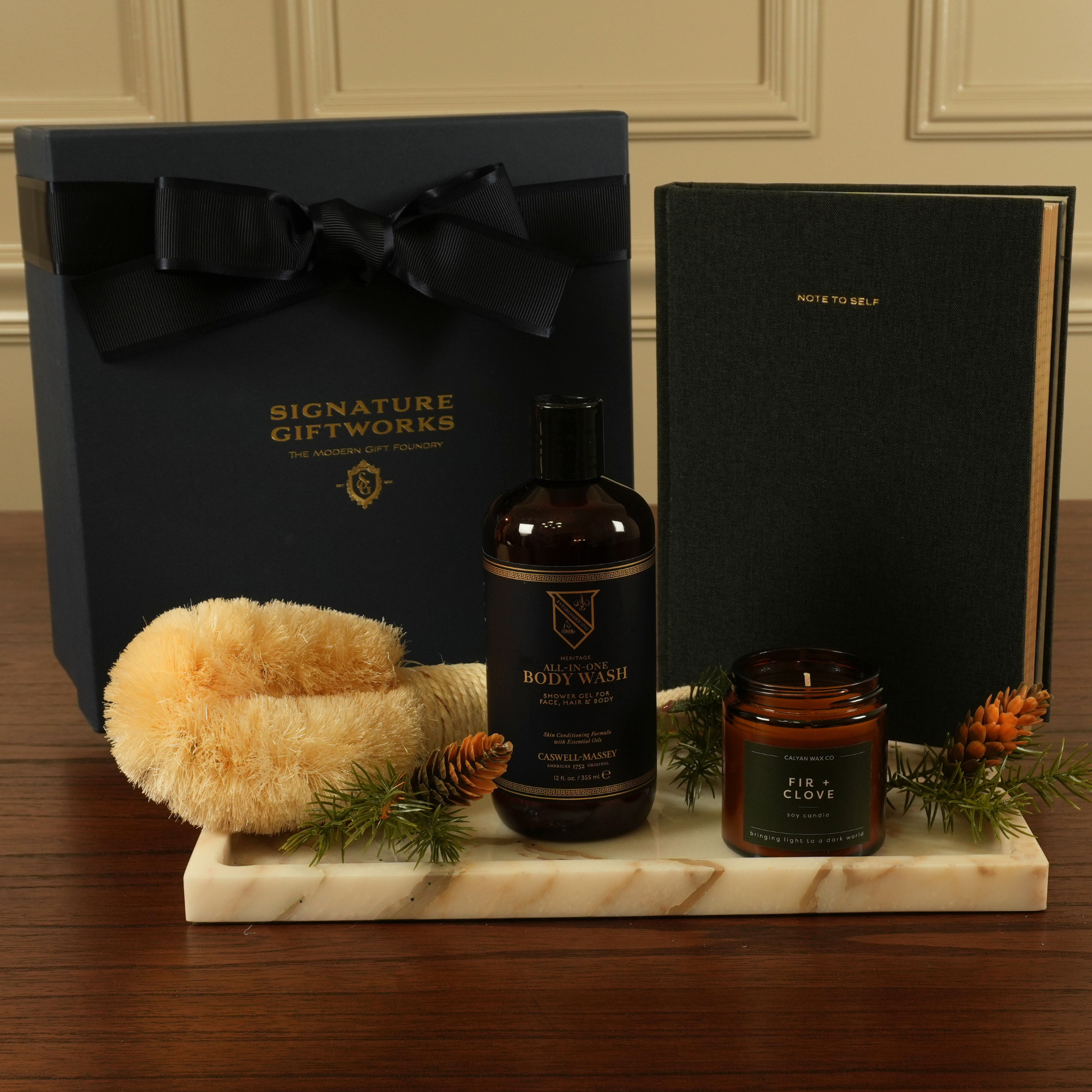 Luxury men’s spa gift set with body wash, sisal body brush, fir-and-clove candle, and linen journal on a marble tray.